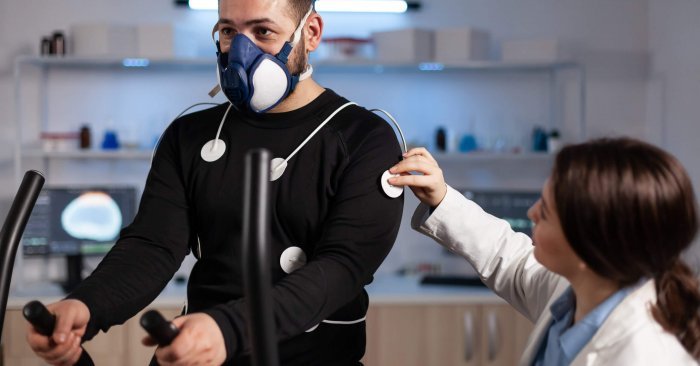 Specialist woman researcher putting electrodes sensor on sportman with mask monitoring EGK data in medical mordern laboratory. Athlete man running on fintess trainer working at body endurance